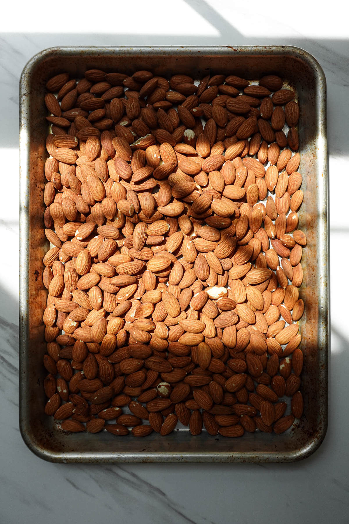 Raw almonds spread on a baking sheet before roasting.