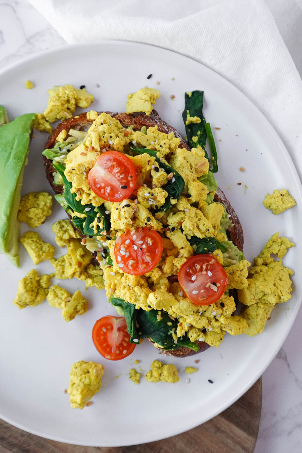 Vegan tofu scramble served on sourdough toast with fresh spinach, cherry tomatoes, and mashed avocado for a healthy and flavorful breakfast.