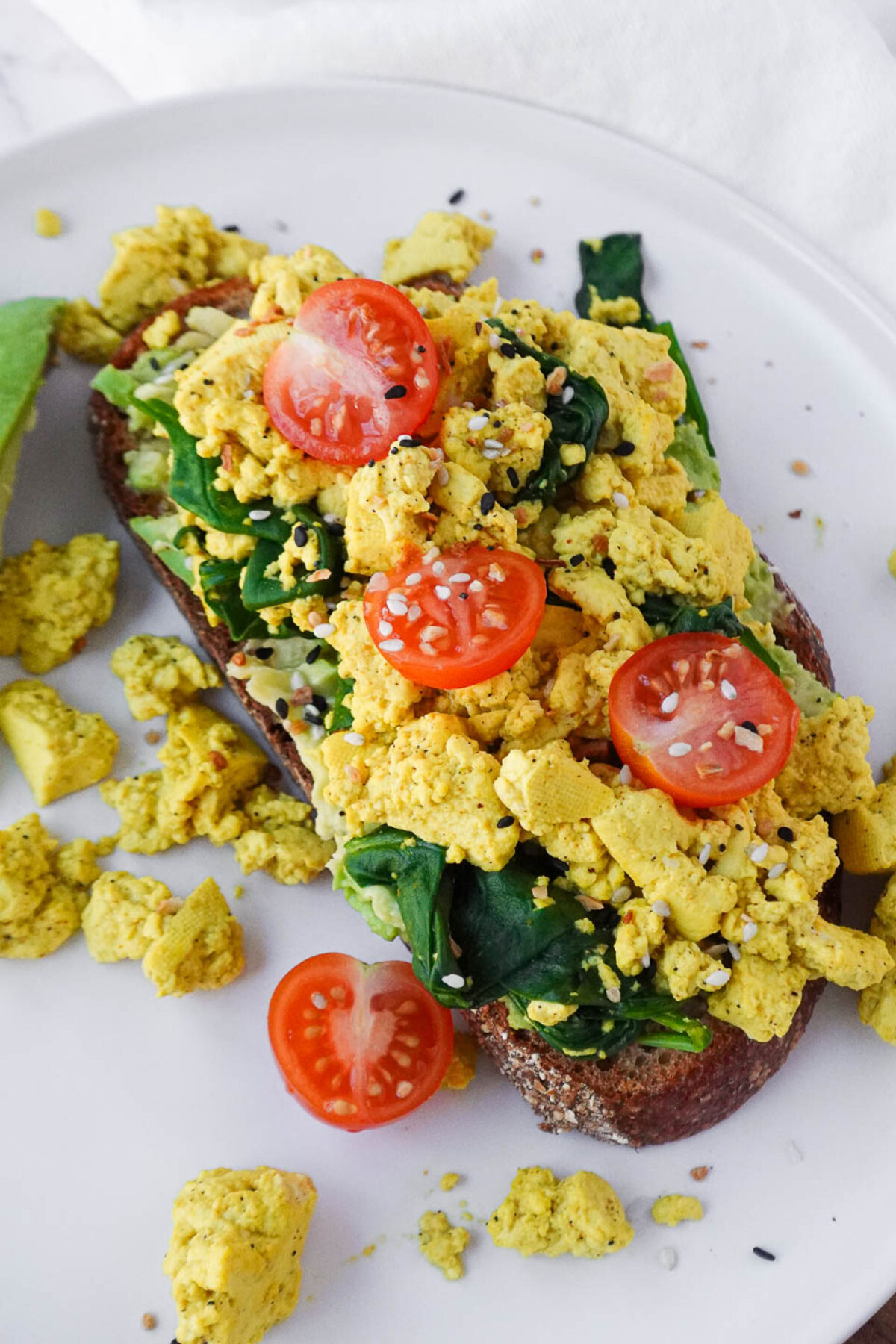 close up of vegan tofu scramble served on sourdough toast with fresh spinach, cherry tomatoes, and mashed avocado for a healthy and flavorful breakfast.