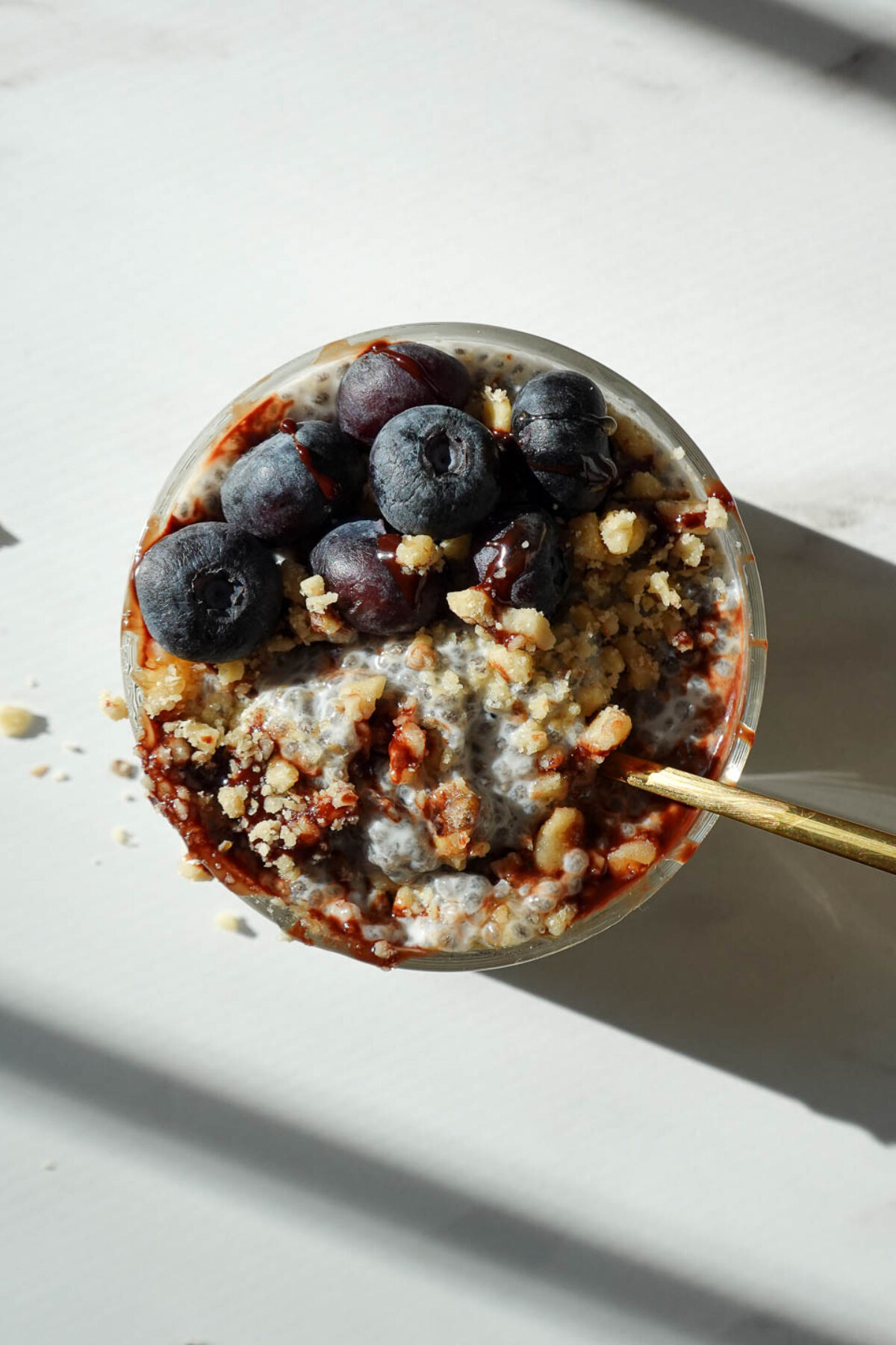 easy chia pudding topped with blueberries and chopped walnuts with a spoon showing it's creamy texture