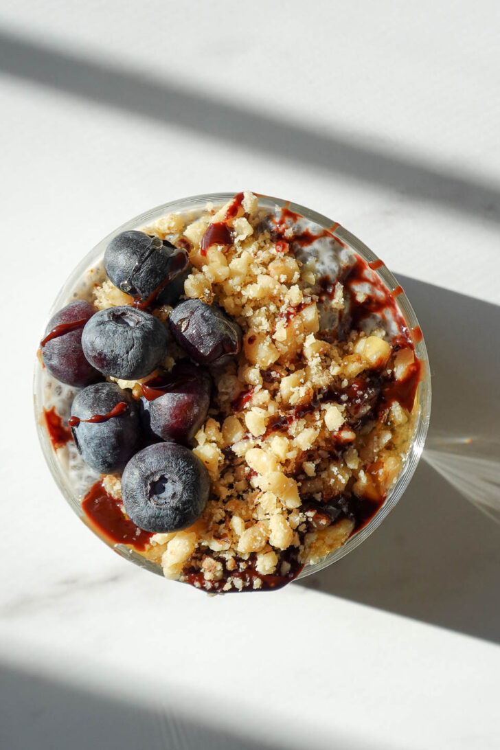 overhead shot of chia pudding topped with blueberries, chopped walnuts, and a drizzle of date syrup