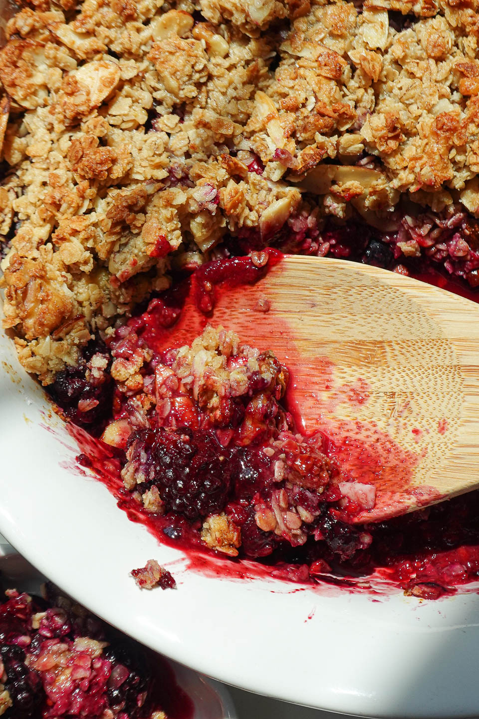 healthy berry crisp made with fruit and a nutty crisp topping being served with a wooden spoon