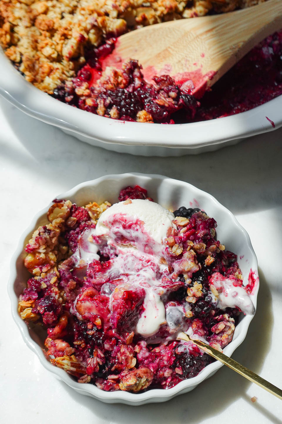 healthy berry crisp in a bowl with swirls of vegan vanilla ice cream