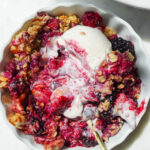 close up of vegan and gluten-free healthy berry crisp in a bowl with swirls of vegan vanilla ice cream