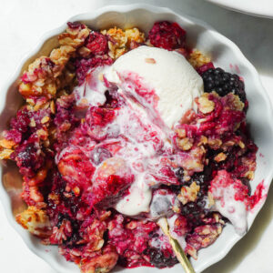 close up of vegan and gluten-free healthy berry crisp in a bowl with swirls of vegan vanilla ice cream
