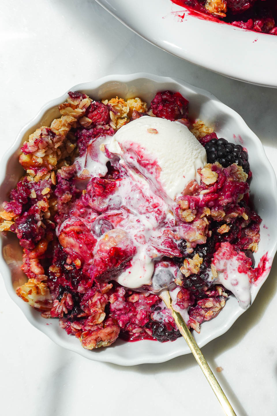 close up of vegan and gluten-free healthy berry crisp in a bowl with swirls of vegan vanilla ice cream