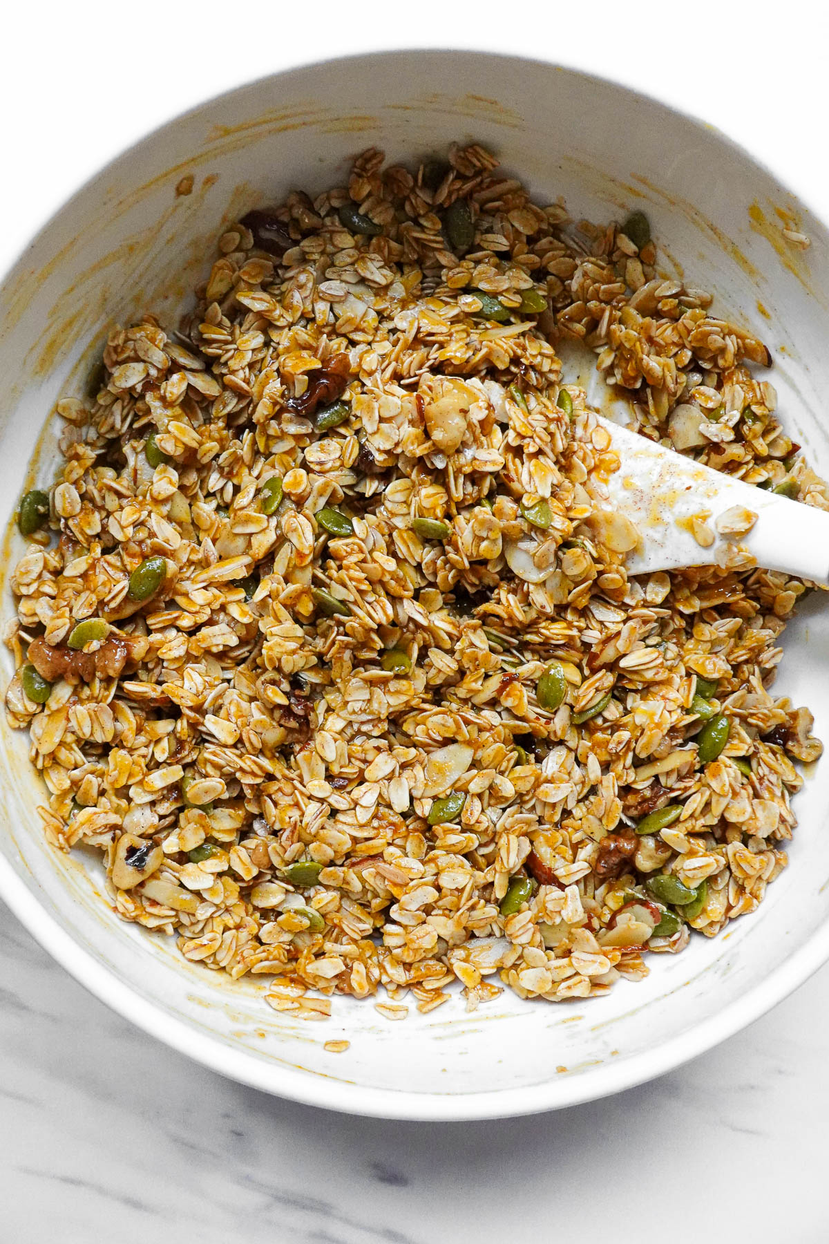 Stirring oats, walnuts, almonds, pepitas, pumpkin pie spice, and salt into the wet ingredients.
