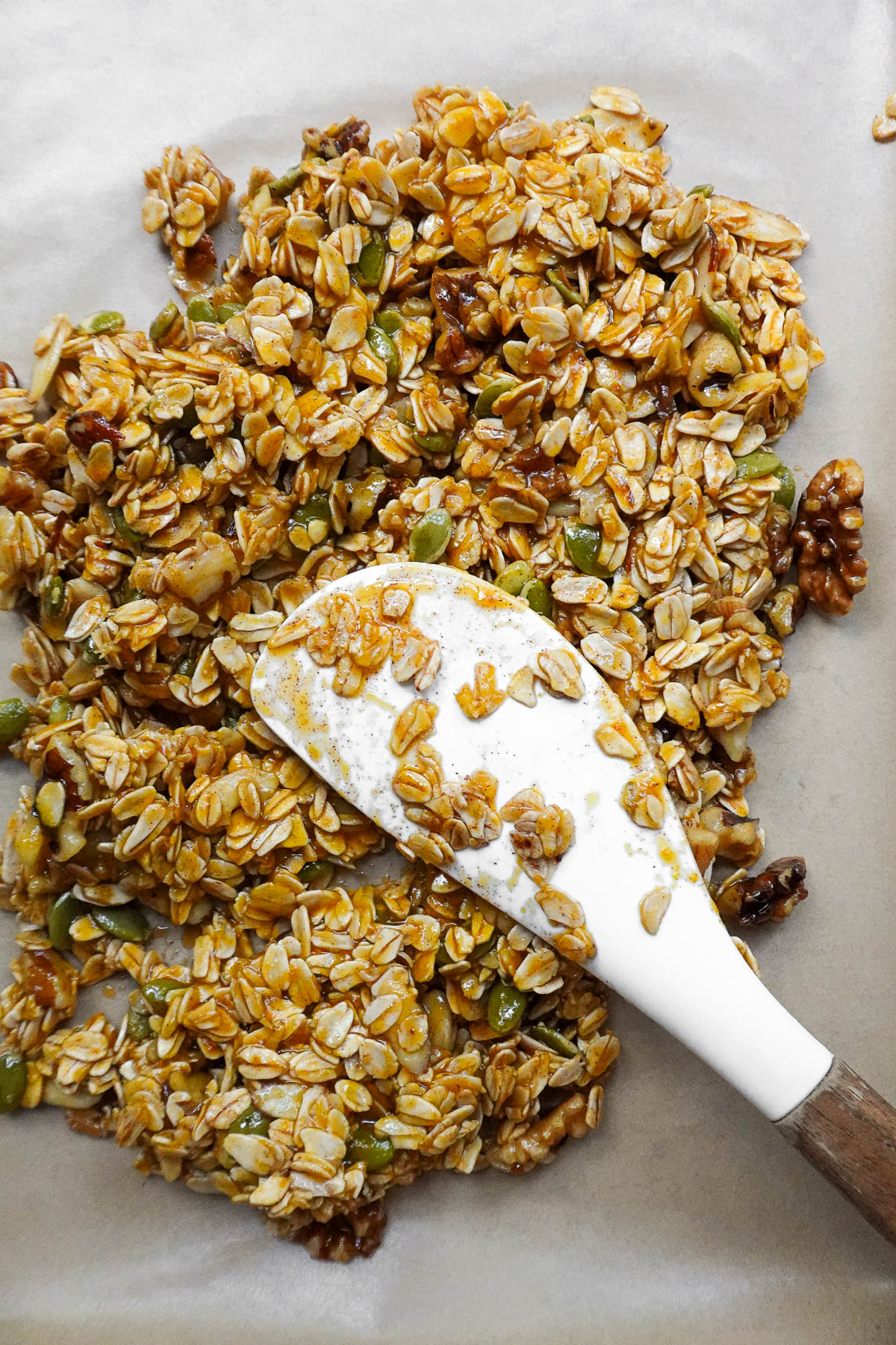 Spreading pumpkin spice granola evenly across a parchment-lined baking sheet before baking.