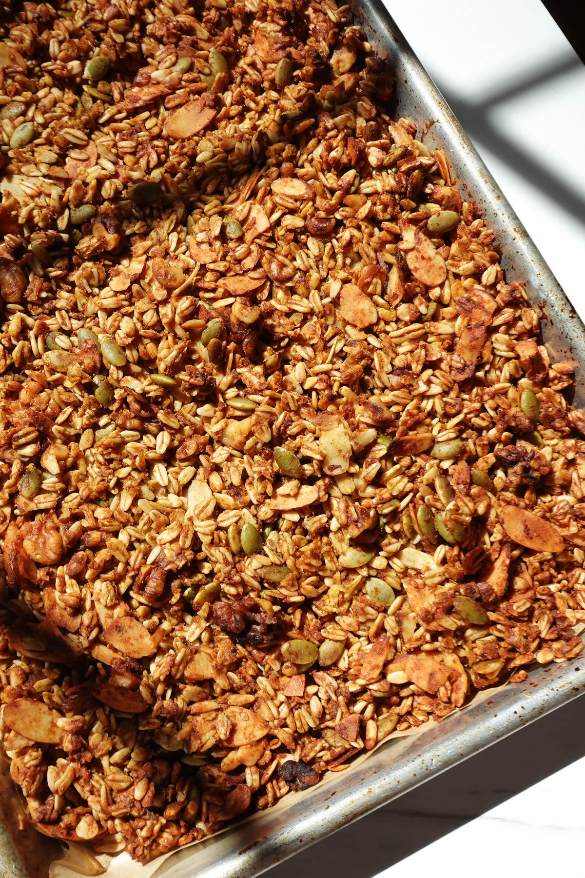 Baked pumpkin spice granola cooling on a baking sheet before breaking into crunchy clusters.