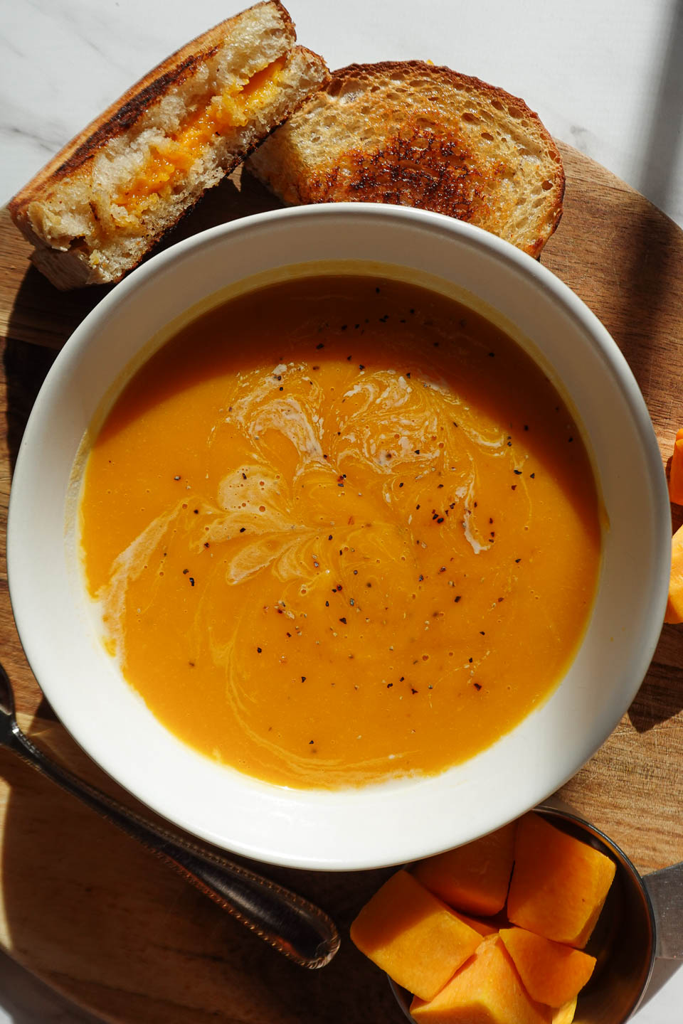 vegan butternut squash soup served in a white bowl with a vegan grilled cheese on the side