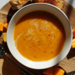 vegan butternut squash soup served in a white bowl with a vegan grilled cheese on the side