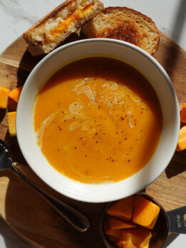 vegan butternut squash soup served in a white bowl with a vegan grilled cheese on the side