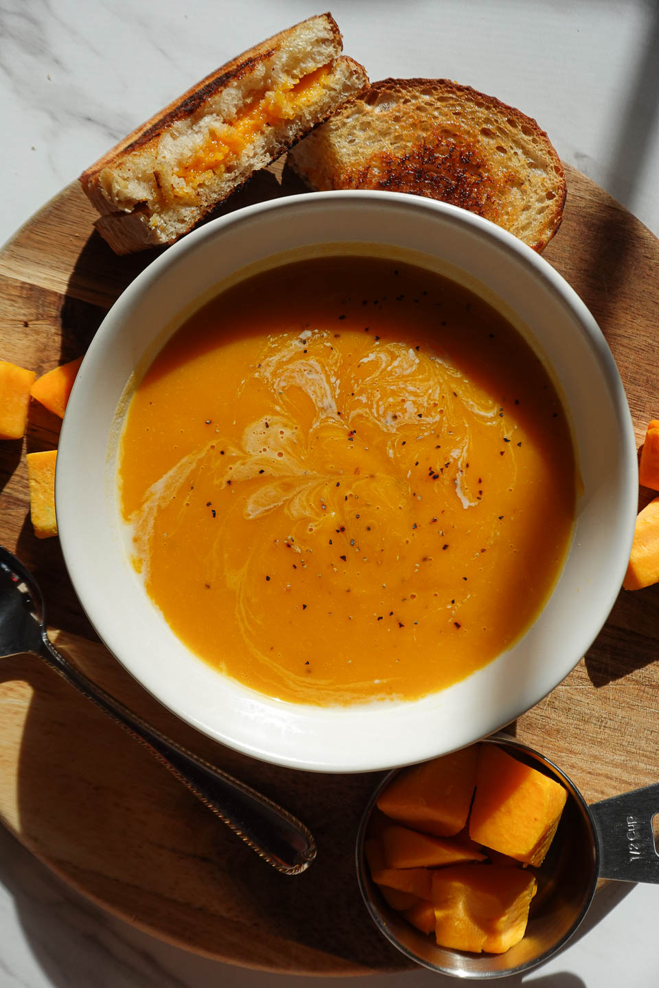vegan butternut squash soup served in a white bowl with a vegan grilled cheese on the side