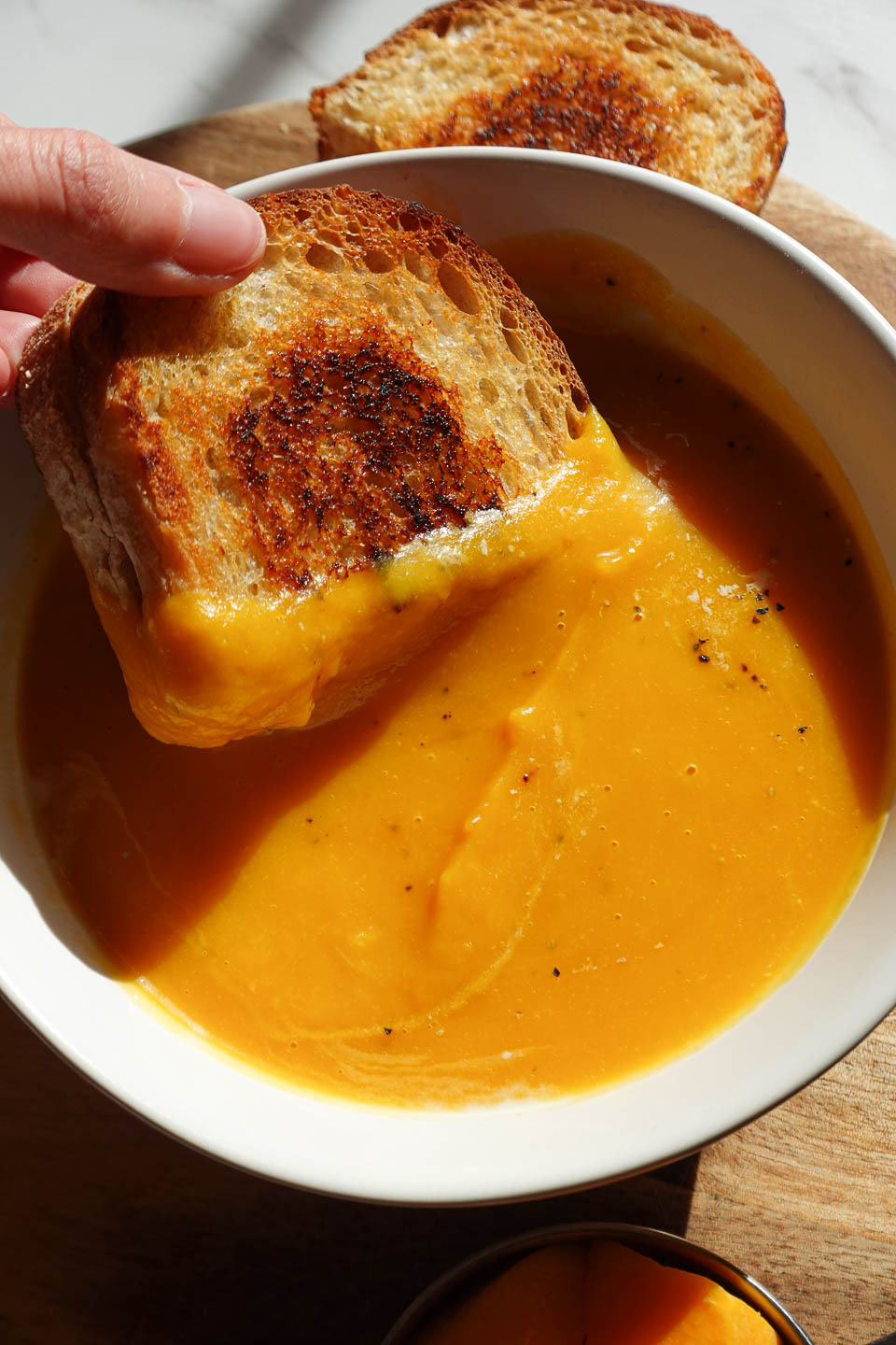 Vegan grilled cheese sandwich dipped into creamy butternut squash soup.