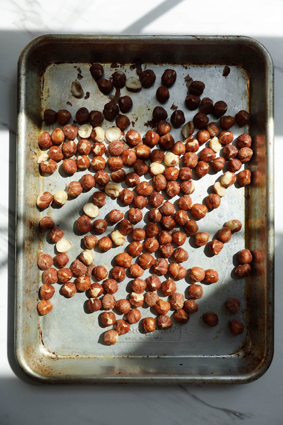 Raw hazelnuts spread on a baking sheet before roasting.