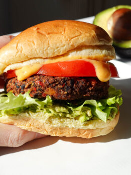 black bean sweet potato veggie burger on a hamburger bun served with guacamole, lettuce, tomato, and dairy-free queso