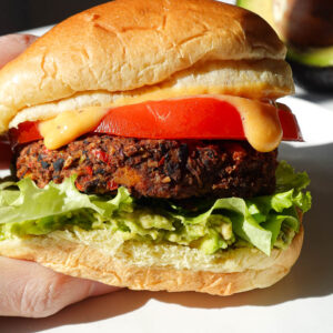 black bean sweet potato veggie burger on a hamburger bun served with guacamole, lettuce, tomato, and dairy-free queso