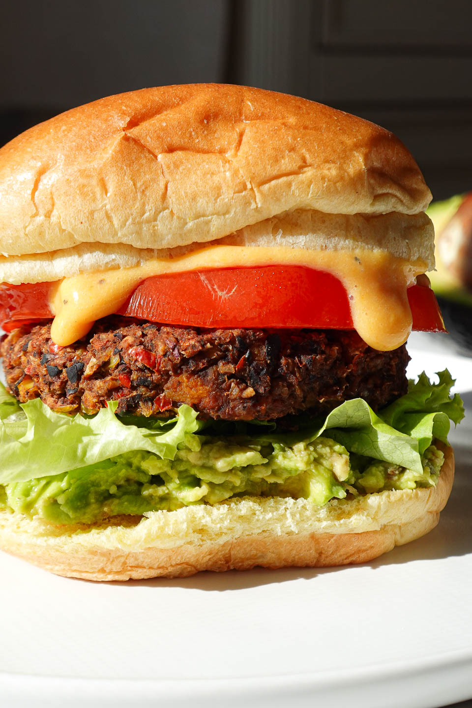 black bean and sweet potato veggie burger served on a plate in a hamburger bun topped with guacamole, lettuce, tomato, and dairy-free queso