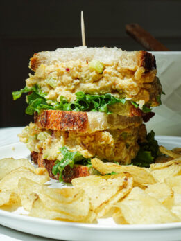 Chickpea salad sandwich cut in half on a plate with potato chips.