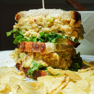 Chickpea salad sandwich cut in half on a plate with potato chips.