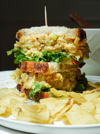 Chickpea salad sandwich cut in half on a plate with potato chips.