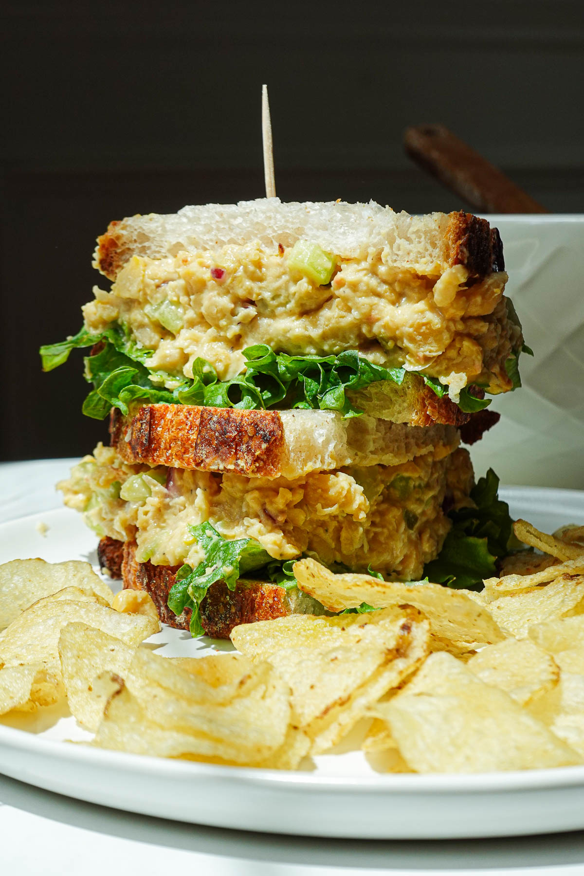 Chickpea salad sandwich cut in half on a plate with potato chips.
