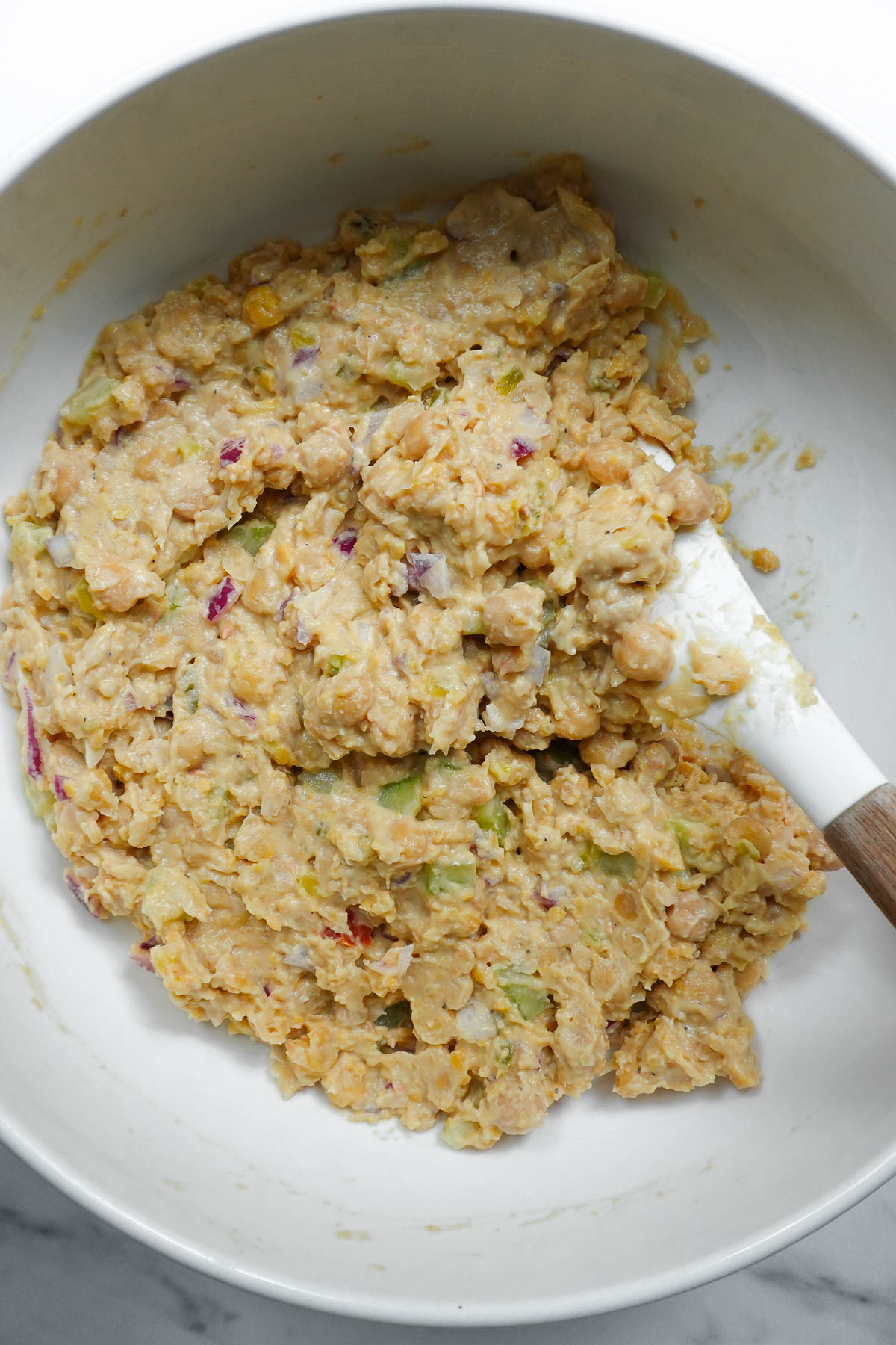 Chickpea salad mixture being stirred together in a mixing bowl.