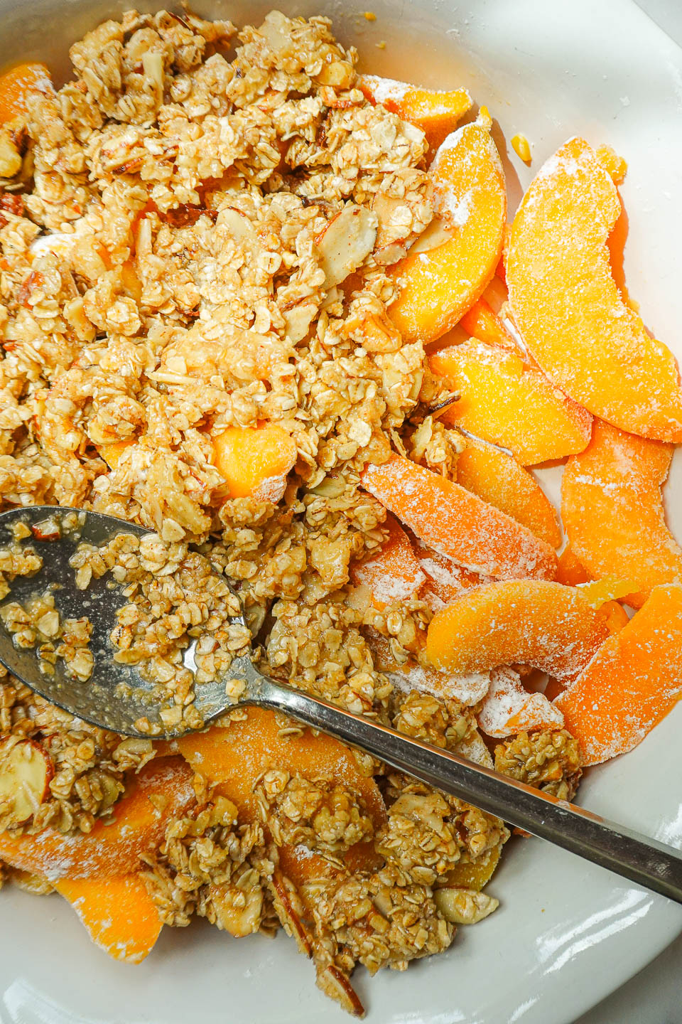 Sprinkling the oat-almond crisp topping evenly over the peach filling.