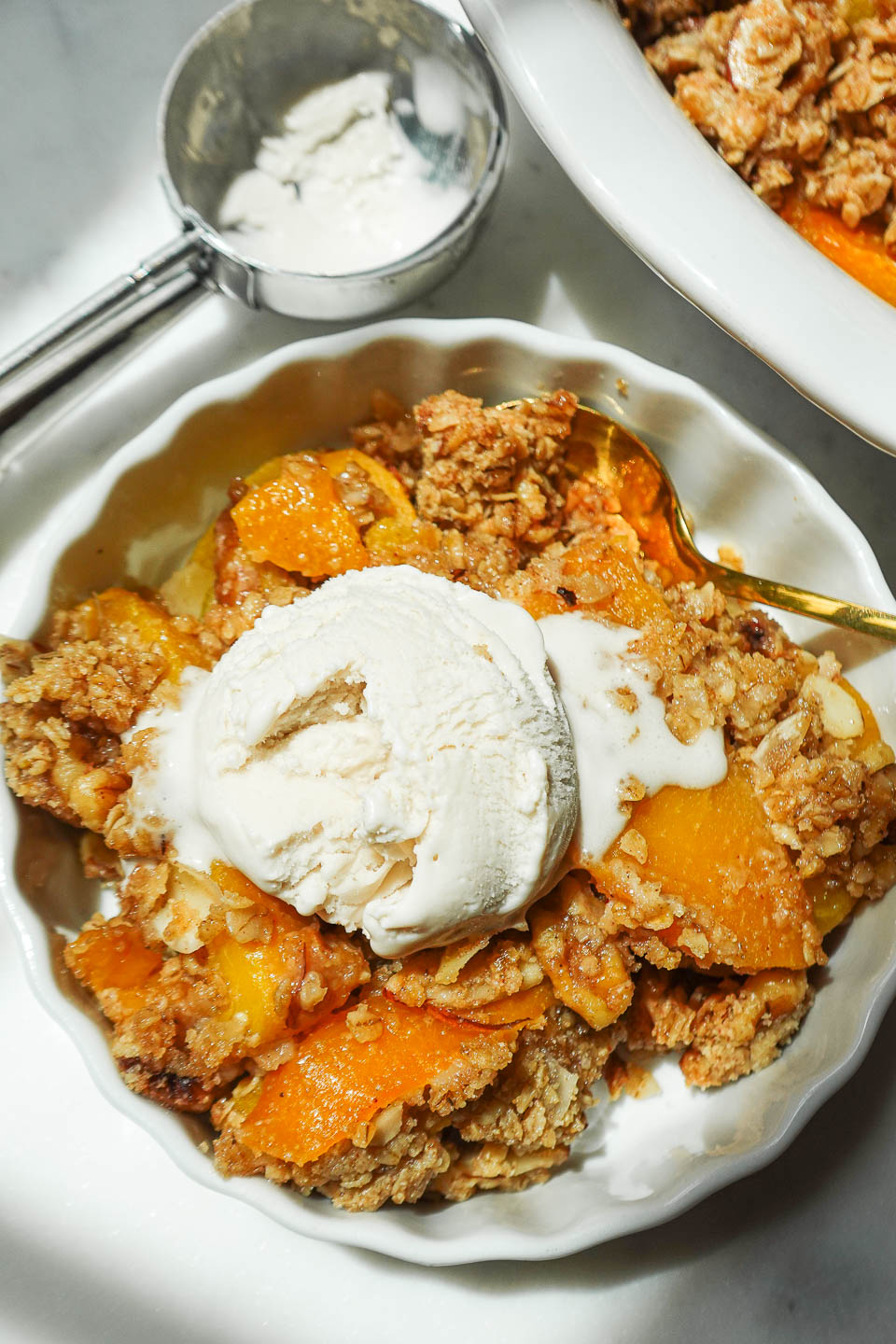 Overhead shot of freshly baked peach crisp topped with a scoop of vegan vanilla ice cream