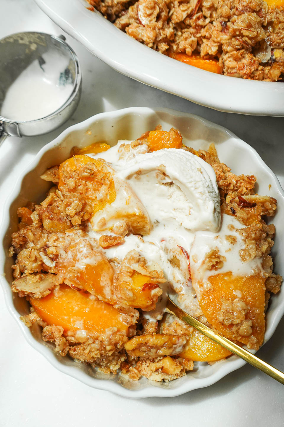 Close up shot of freshly baked peach crisp topped with a scoop of vegan vanilla ice cream