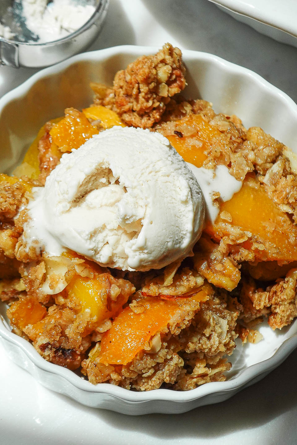 Close up shot of healthy vegan peach crisp topped with a scoop of vegan vanilla ice cream