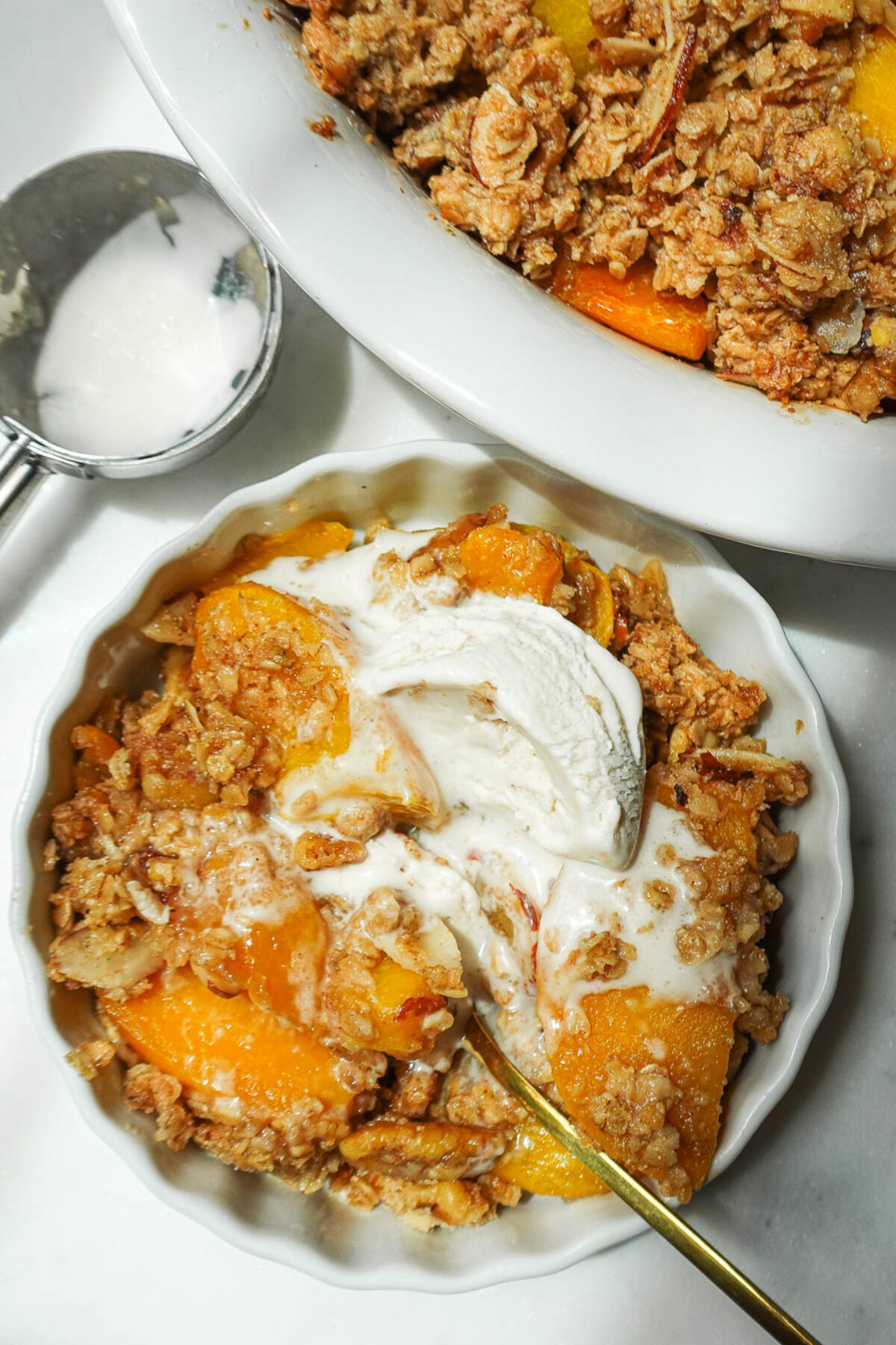 Overhead shot of freshly baked peach crisp topped with a scoop of vegan vanilla ice cream