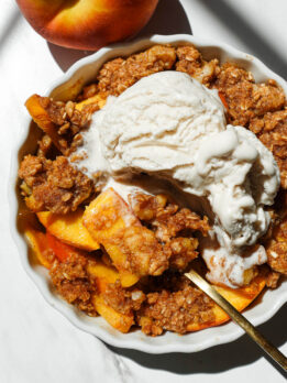 Single serve healthy peach crisp in a white ramekin topped with golden oat-nut crumble