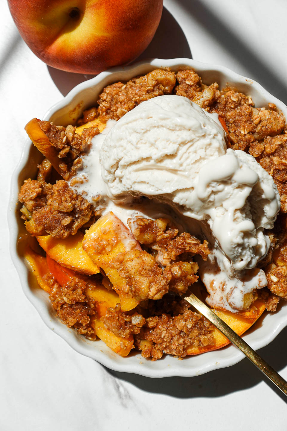 Single serve healthy peach crisp in a white ramekin topped with golden oat-nut crumble