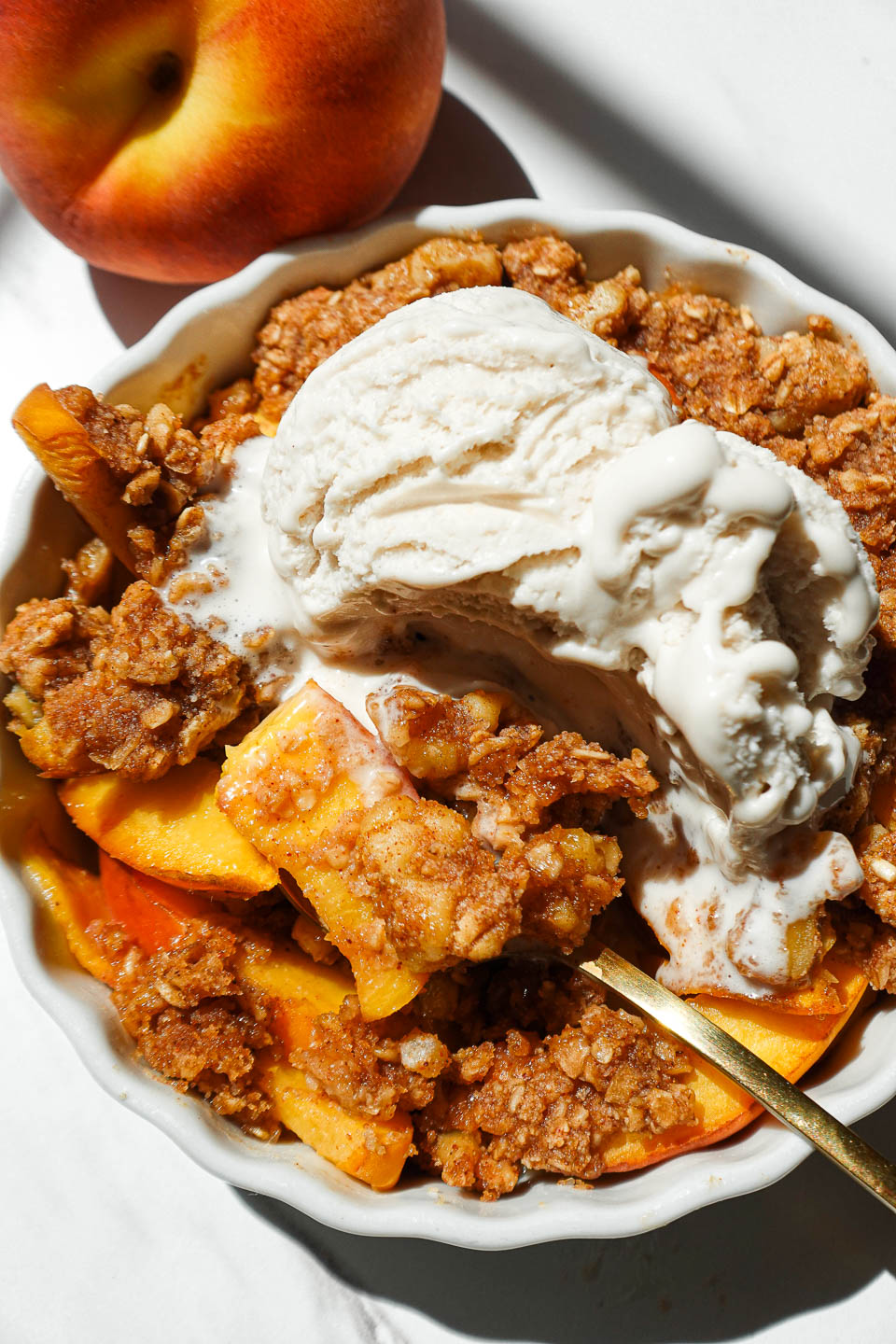 Healthy single serve peach crisp with juicy baked peaches and nutty crisp topping in a ramekin with a spoon