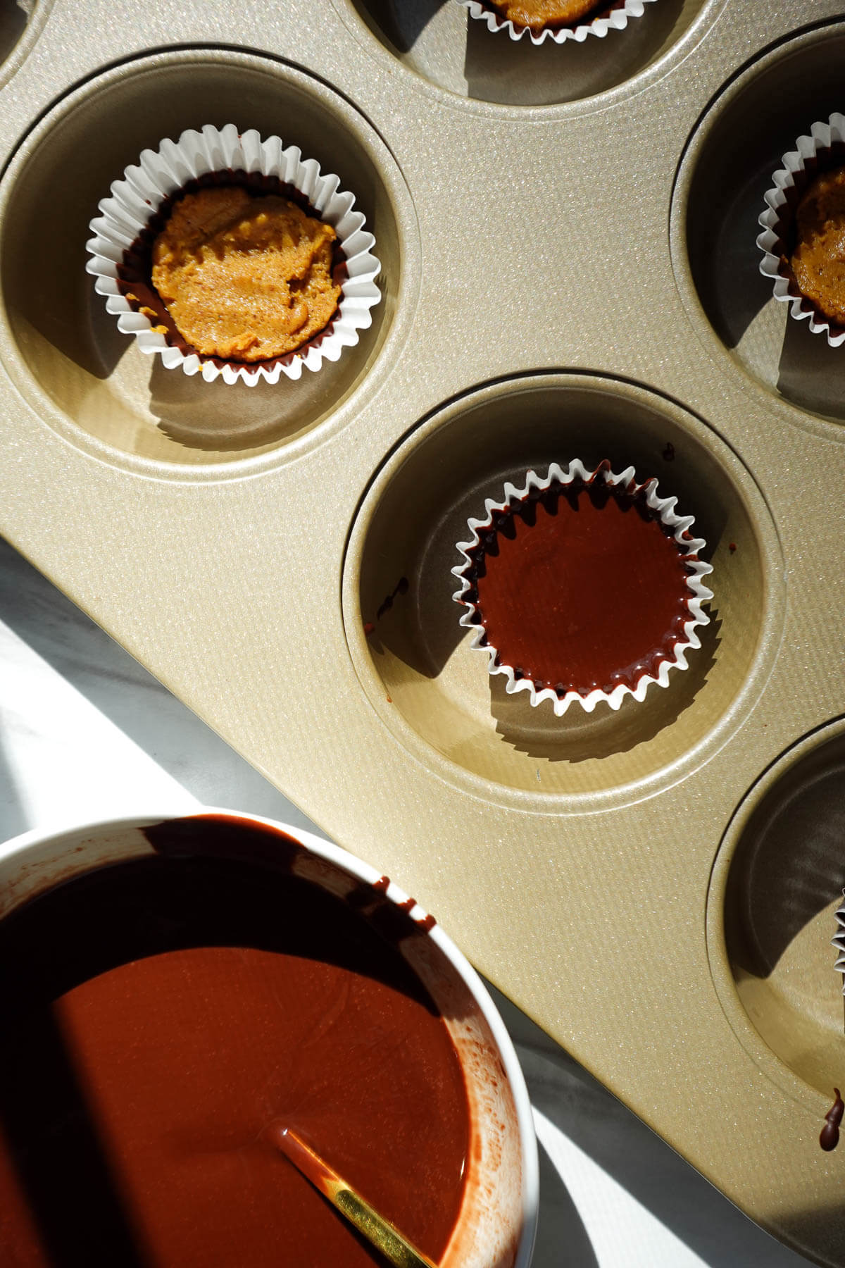 Adding a top layer of chocolate to pumpkin peanut butter cups.