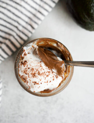 Creamy chocolate avocado pudding in a jar topped with coconut whipped cream and chocolate shavings.