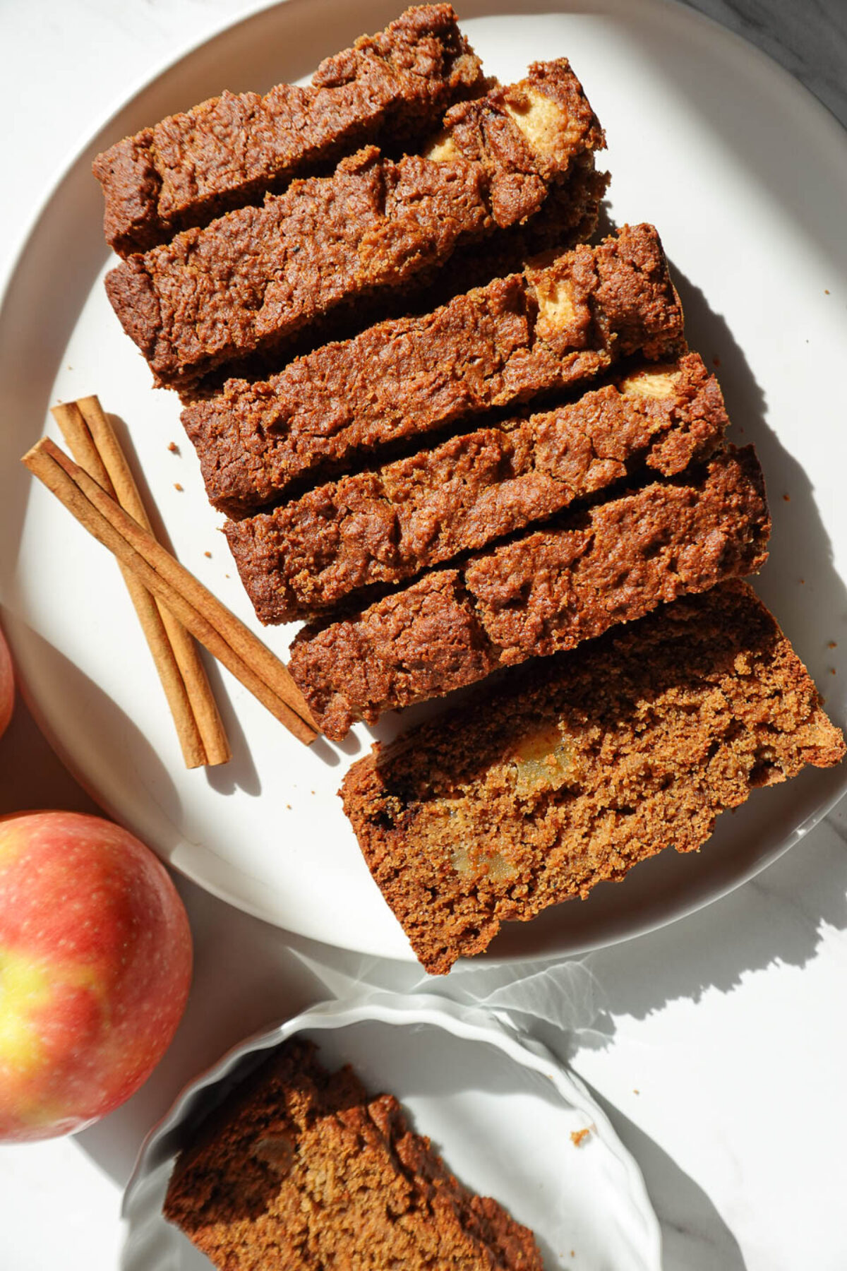healthy apple bread sliced on a plate with apples in the background