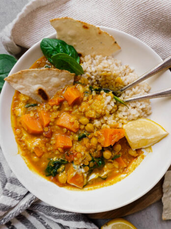 close up shot of Chickpea, Sweet Potato and Lentil Curry with naan, lemon wedge and spoons