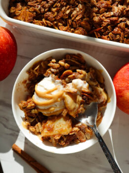 Healthy apple crisp served in a bowl topped with vanilla ice cream.