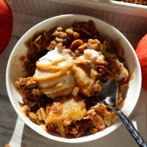 Healthy apple crisp served in a bowl topped with vanilla ice cream.