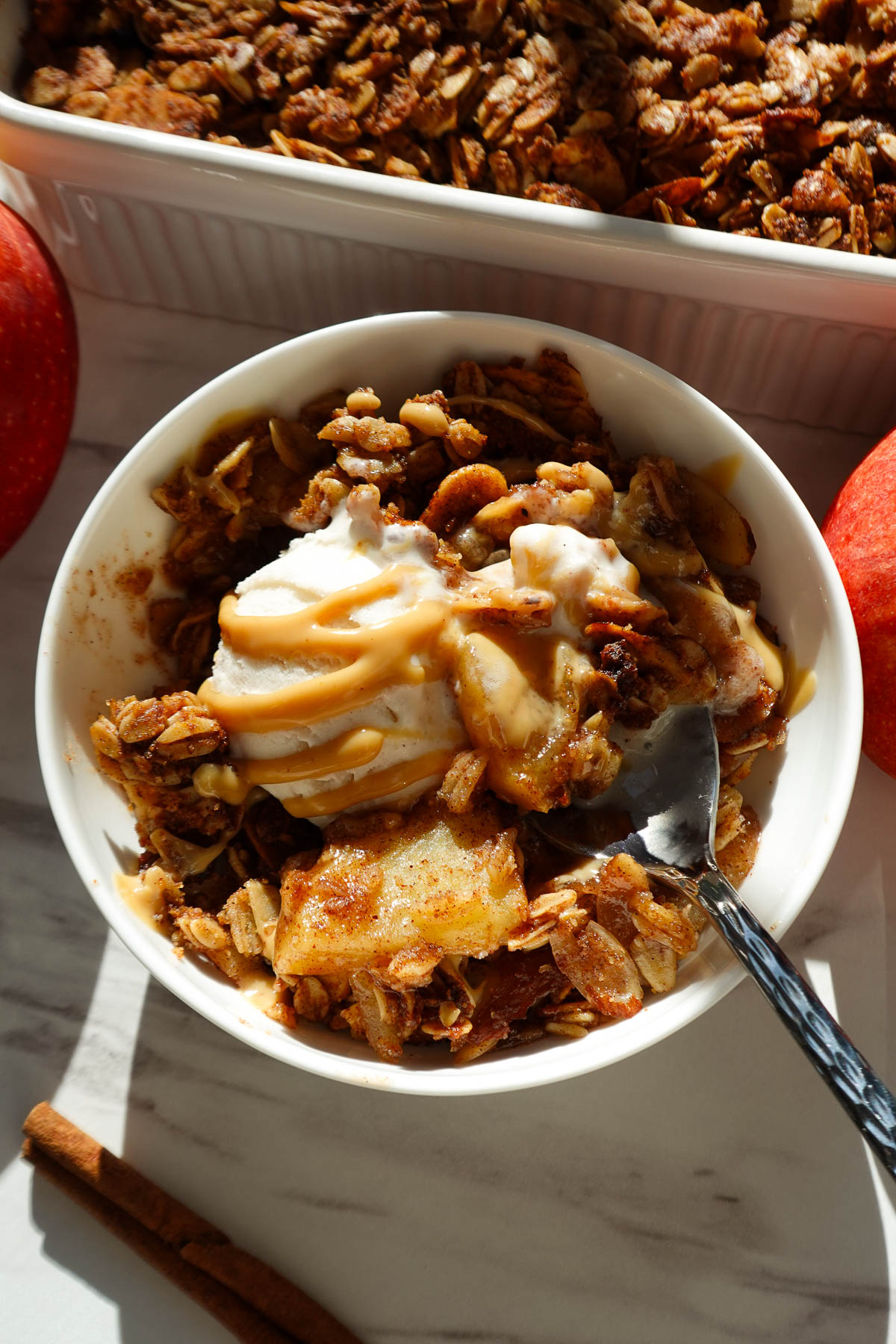 Healthy apple crisp served in a bowl topped with vanilla ice cream and drizzle of peanut butter.