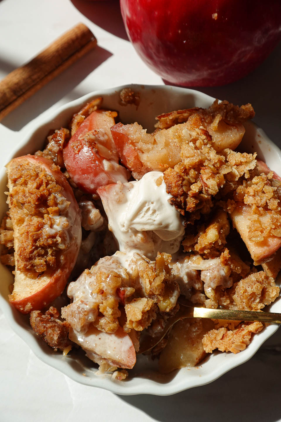 close up of vegan apple crisp served in a bowl with vanilla ice cream