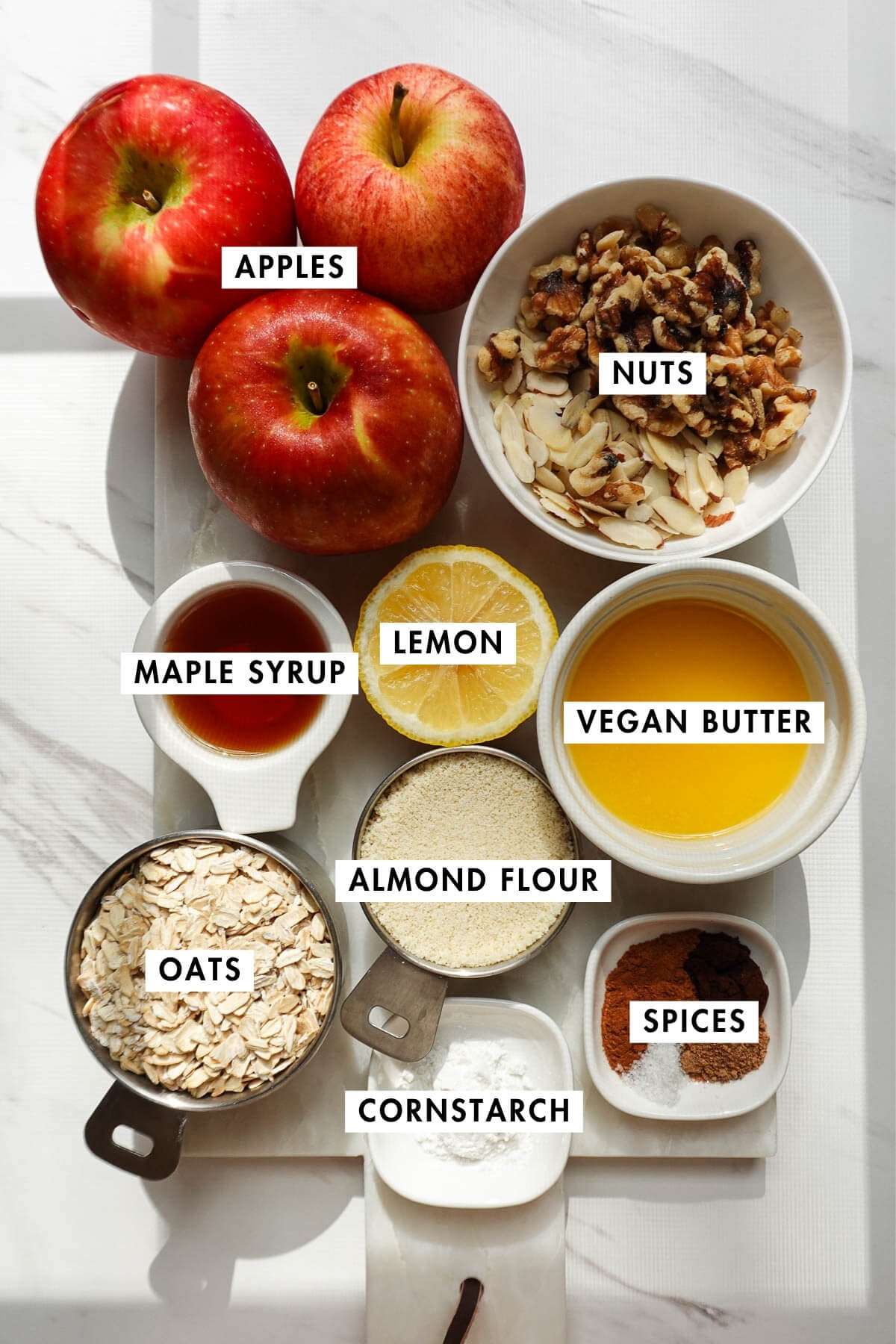 Measured and labeled ingredients needed to make vegan apple crisp, including apples, oats, cinnamon, and maple syrup.