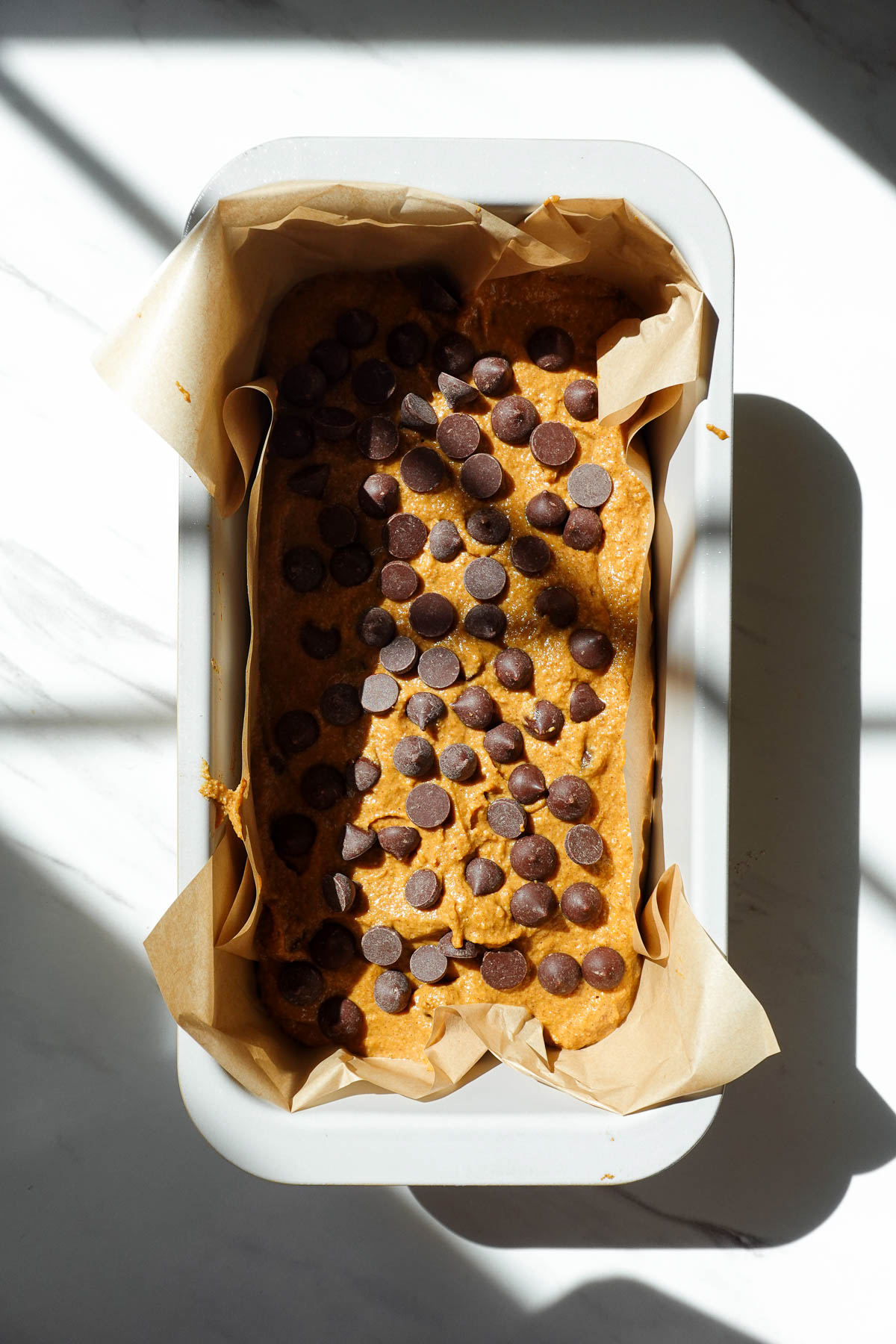 Vegan pumpkin bread batter in a parchment-lined loaf pan topped with chocolate chips.