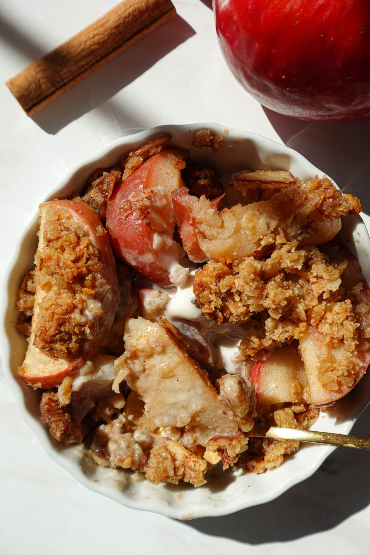 Single serve healthy apple crisp in a white ramekin topped with golden oat and nut crumble, served warm with a scoop of vegan vanilla ice cream.