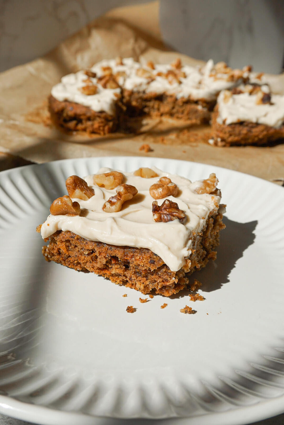 slice of healthy carrot cake on a plate and topped with vegan cream cheese frosting and chopped walnuts