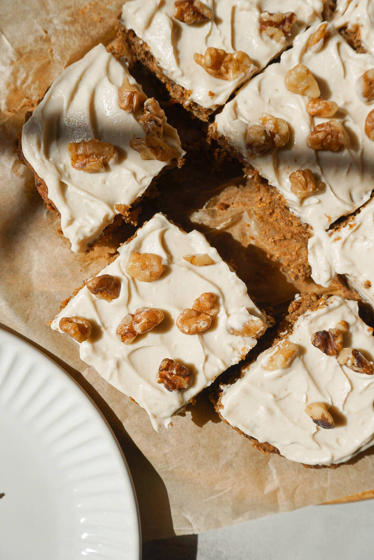 overhead shot of healthy carrot cake sliced and topped with vegan cream cheese frosting and chopped walnuts