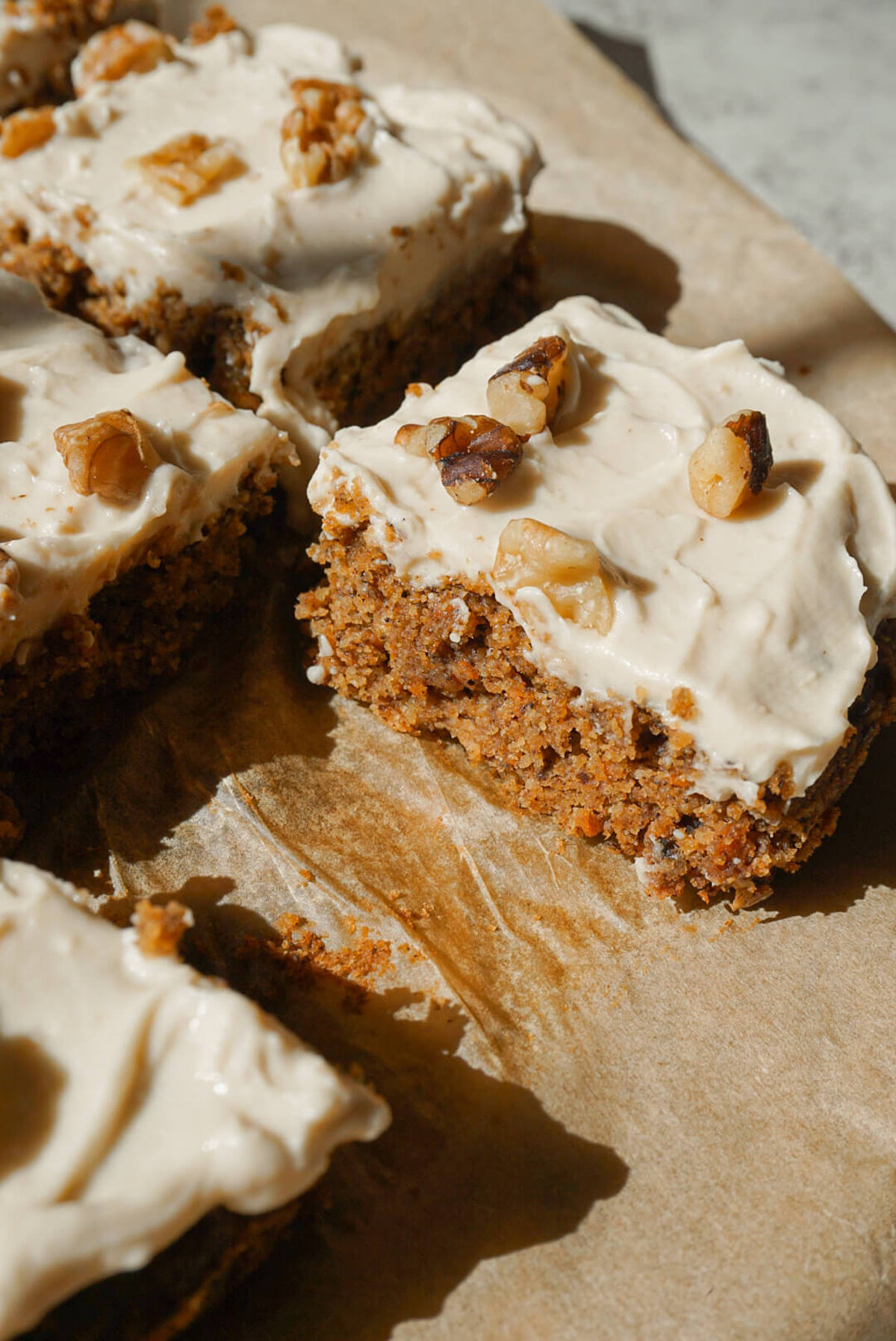 healthy carrot cake sliced and topped with vegan cream cheese frosting and chopped walnuts showcasing it's moist and fluffy texture