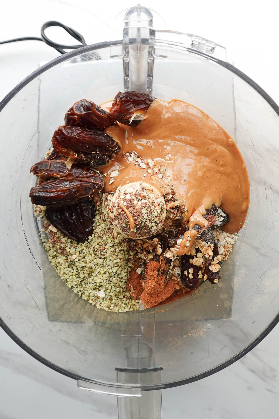 Medjool dates, peanut butter, oats, and seeds being blended in a food processor to make energy ball mixture